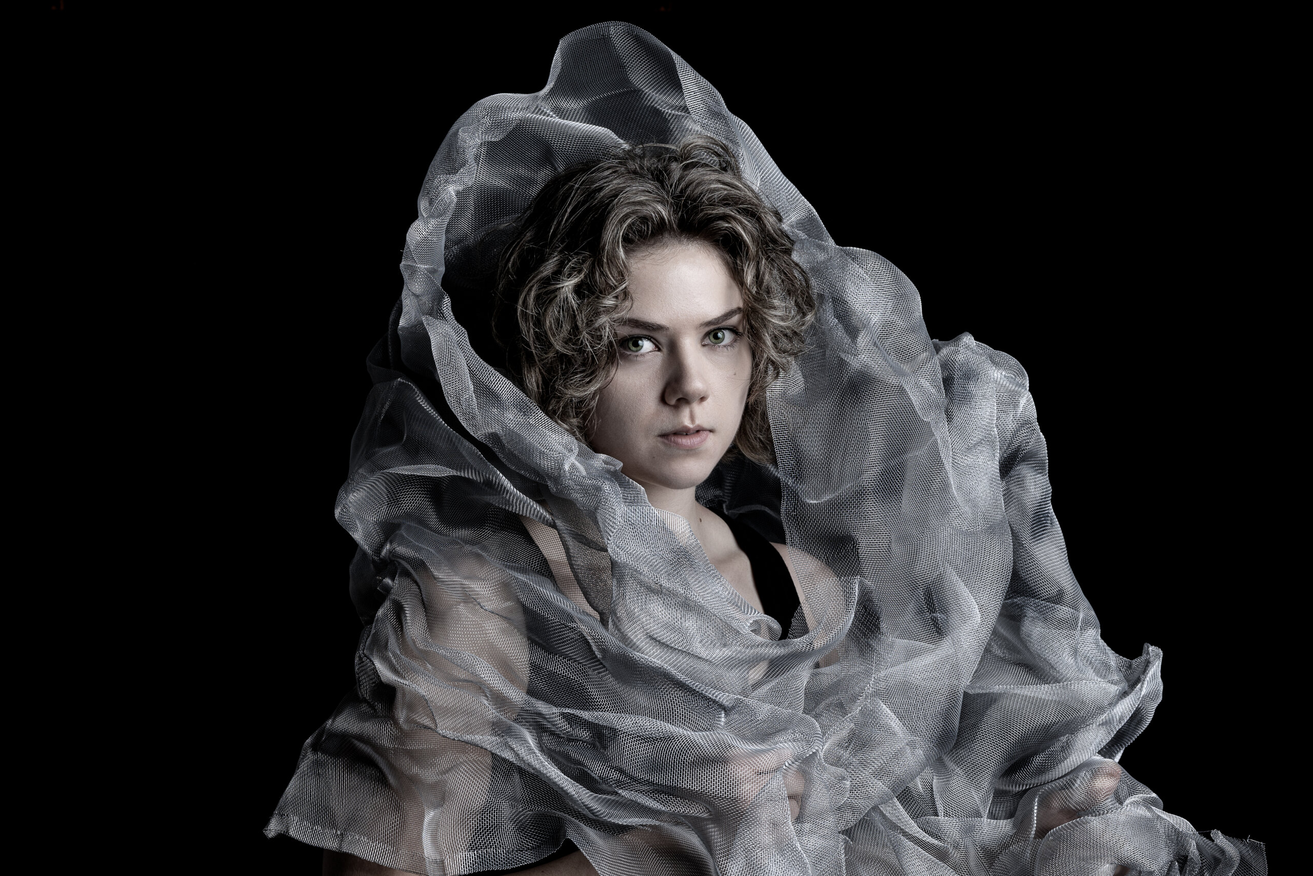 Model ist umgeben von einem Fliegengitter. Ihre Augen leuchten Grün. Ihr Blick ist ernst.